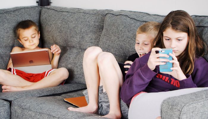 Children lying on the sofa and using gadgets.— Pexels