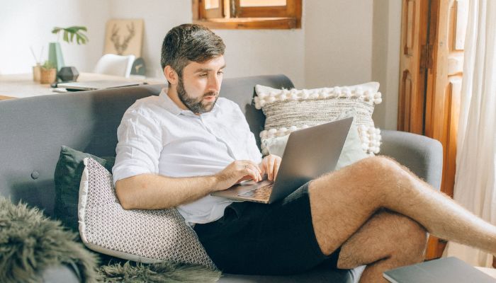 The image shows a man sitting on a couch, using a laptop. — Pexels
