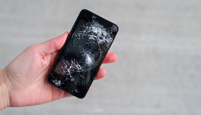 An undated image of a person holding a broken phone. — Canva