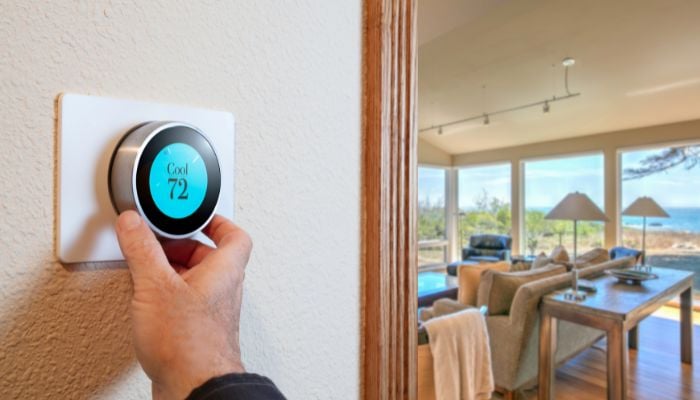 An undated image illustrating a person adjusting a digital thermostat. — Canva