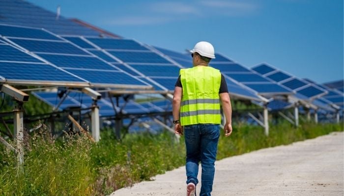 An undated image illustrating a person is passing by solar panels. — Canva