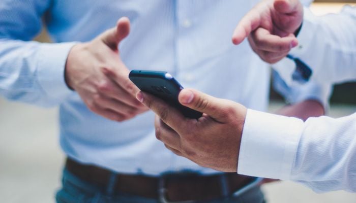The image shows a man showing a phone to another man.— Unsplash
