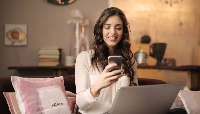 The image shows a woman smiling at her phone. — Pexels