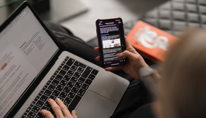 A representational image shows a woman using his mobile besides a laptop. — Unsplash