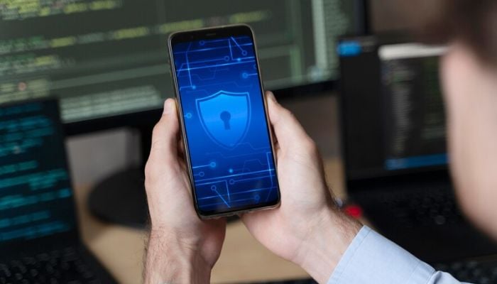 The image shows a person using a smartphone with a security lock symbol on it. — Freepik