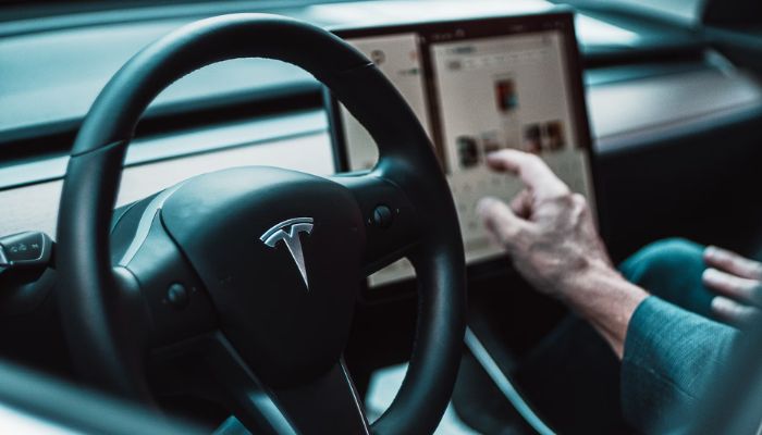 The image shows a Tesla steering wheel. — Unsplash