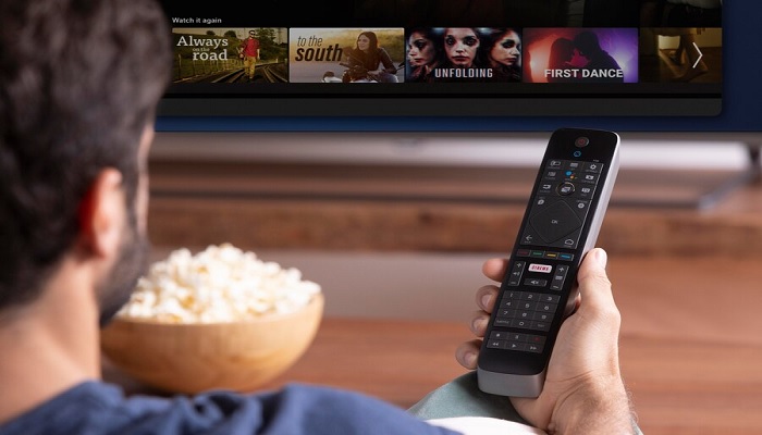 The image shows a person holding a remote and watching TV with popcorn. — Freepik