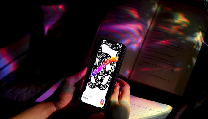 The image shows Threads logo displayed on a mobile held by a person. — Unsplash