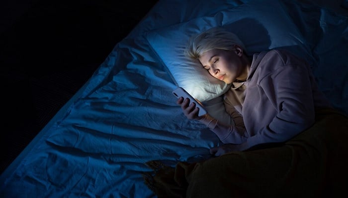 The image shows a woman using her phone in bed at night. — Freepik
