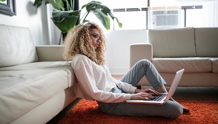 The image shows a woman using a laptop on her lap. — Unsplash