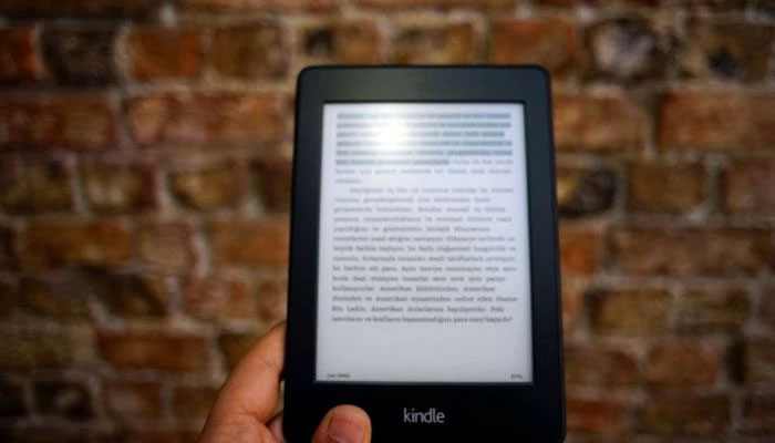 The image shows a person holding an Amazon Kindle Ebook. — Pexels.