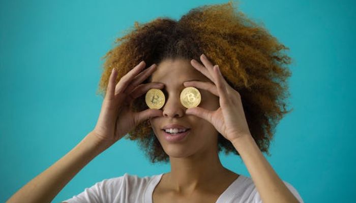 The image shows a woman holding Bitcoins to her eyes. — Pexels