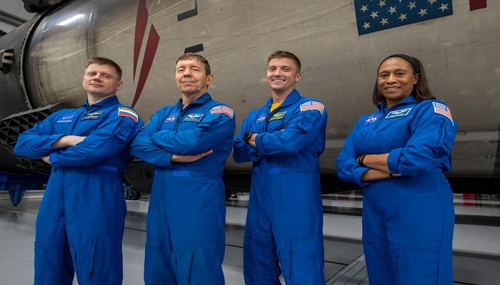 Russian cosmonaut Alexander Grebenkin, pilot Michael Barratt, commander Matthew Dominick, and astronaut Jeanette Epps pose with a Falcon 9 rocket inside SpaceXs hangar in Florida. — SpaceX