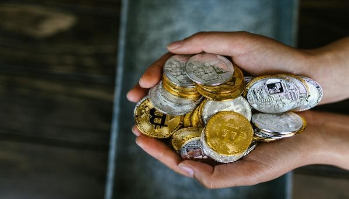The image shows a person holding gold and silver bitcoins. — Pexels