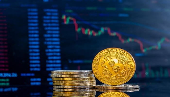 The image shows an artists imagination of a bitcoin in front of a trading screen. — Freepik