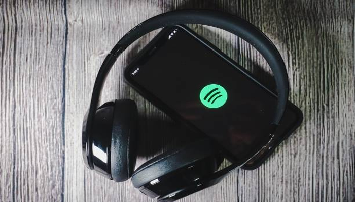 An undated image of Spotify logo on a mobile screen, along with headphones placed on a table. — iStock