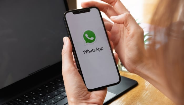 An undated image of a person using a using a phone where a WhatsApp logo is shown. — Canva